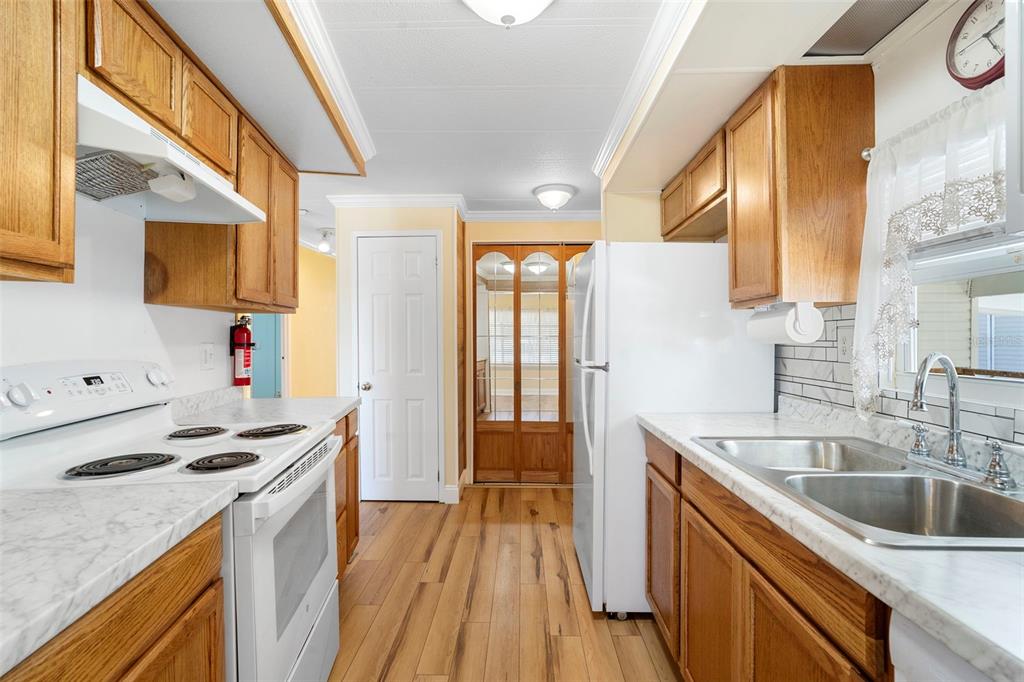 A kitchen features wood cabinets, white appliances, marble-look countertops, and light wood-style flooring — 105 FLORENCE BOULEVARD, DEBARY, FL