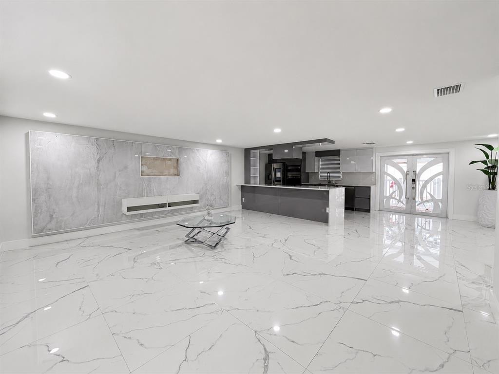A modern open-concept living area features white marble tile flooring and a large marble accent wall — 15810 SEA OATS PLACE, TAMPA, FL