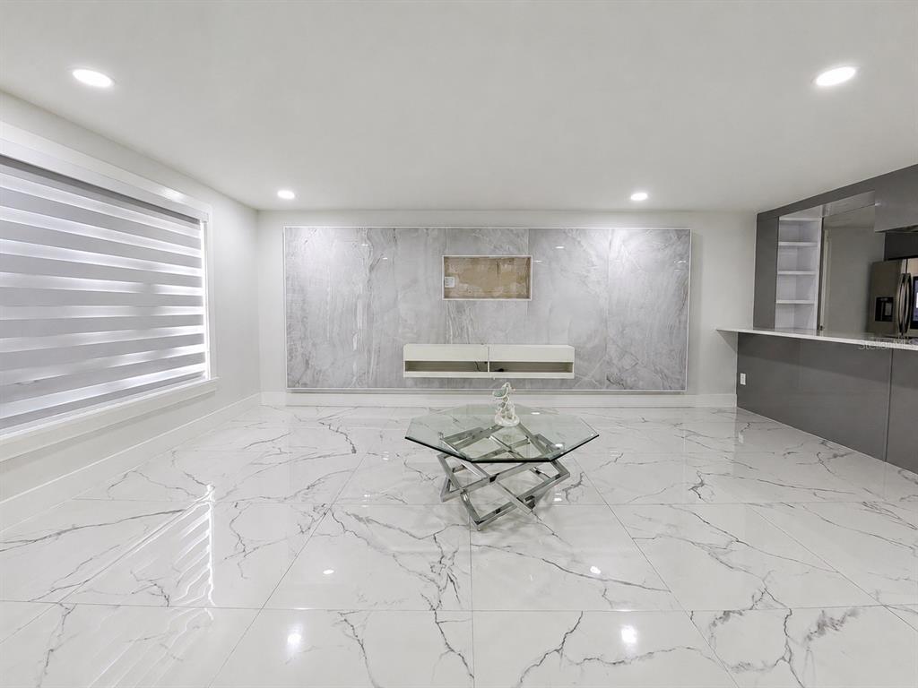 A modern living room features white marble-look tile flooring, a marble accent wall, and glass table — 15810 SEA OATS PLACE, TAMPA, FL