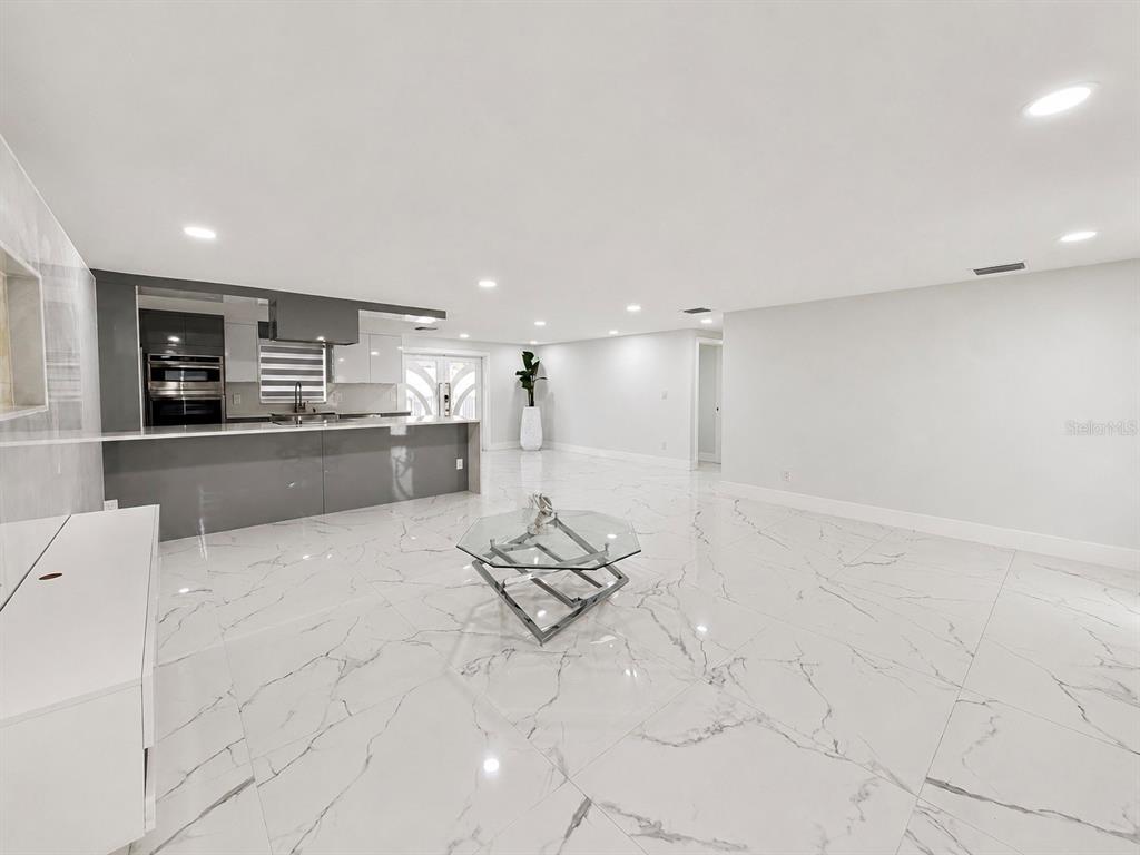 A modern, open-concept living area features white marble-look tile floors and a gray kitchen island — 15810 SEA OATS PLACE, TAMPA, FL