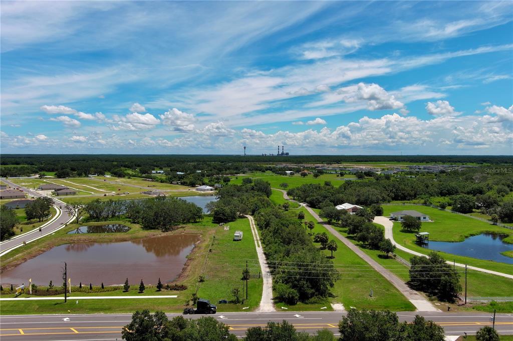 An aerial view shows a rural landscape with ponds, trees, roads, and distant industrial structures — 15820 COUNTY ROAD 675, PARRISH, FL