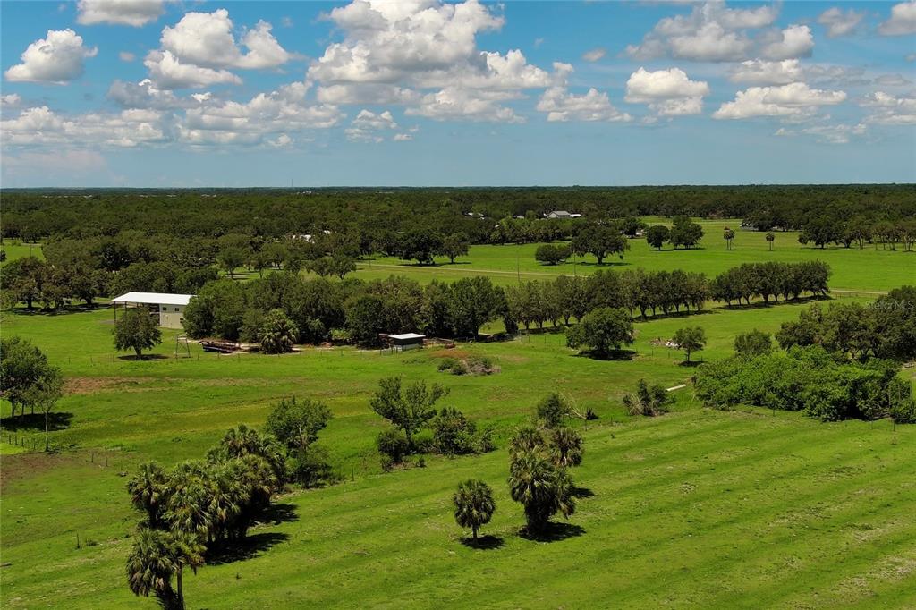 An aerial view of a large, flat, grassy pasture with scattered trees and small buildings — 15820 COUNTY ROAD 675, PARRISH, FL