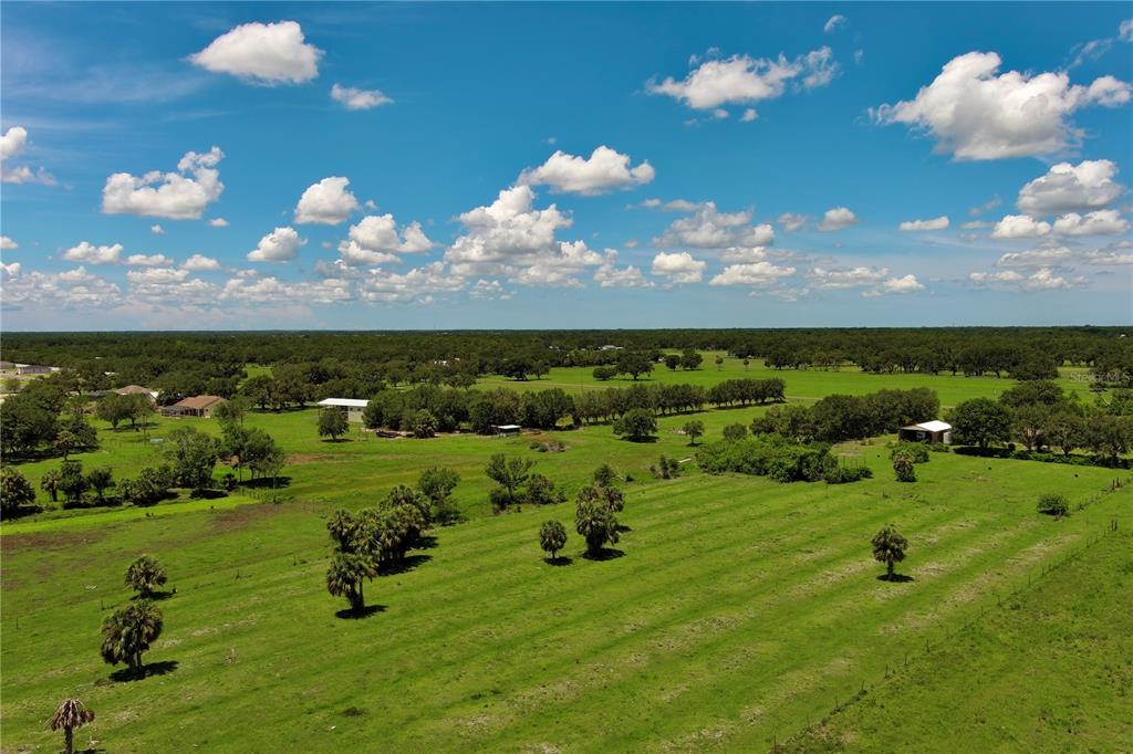 An aerial view of a large, flat, green pasture with scattered trees and distant buildings — 15820 COUNTY ROAD 675, PARRISH, FL