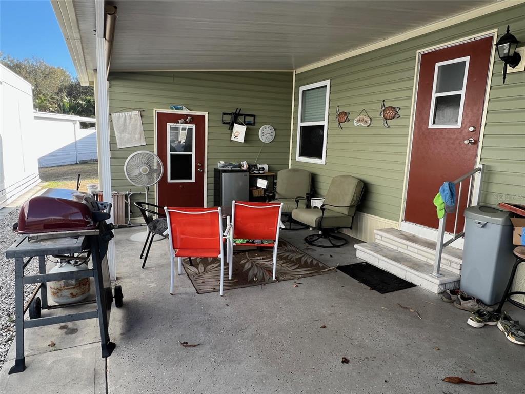 A covered patio features a grill, outdoor seating, and two red doors on a green home — 8300 SEMINOLE BOULEVARD UNIT 218, SEMINOLE, FL