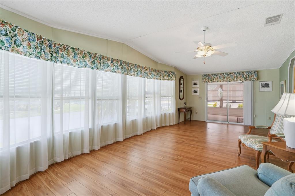 A living room features light wood-look flooring, large windows with floral valances, and a ceiling fan — 452 SHARKS POINT, NORTH PORT, FL