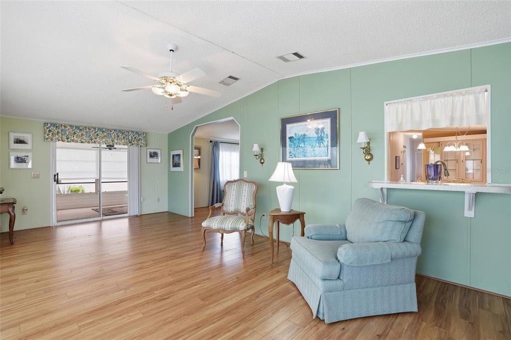 A living room with light green walls, wood-look flooring, a ceiling fan, and a pass-through window — 452 SHARKS POINT, NORTH PORT, FL