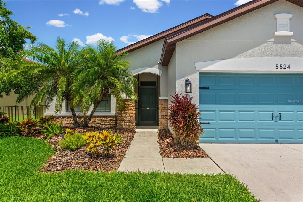 A single-story house exterior features a blue garage door, stone accents, and a palm tree — 5524 107TH TERRACE E, PARRISH, FL