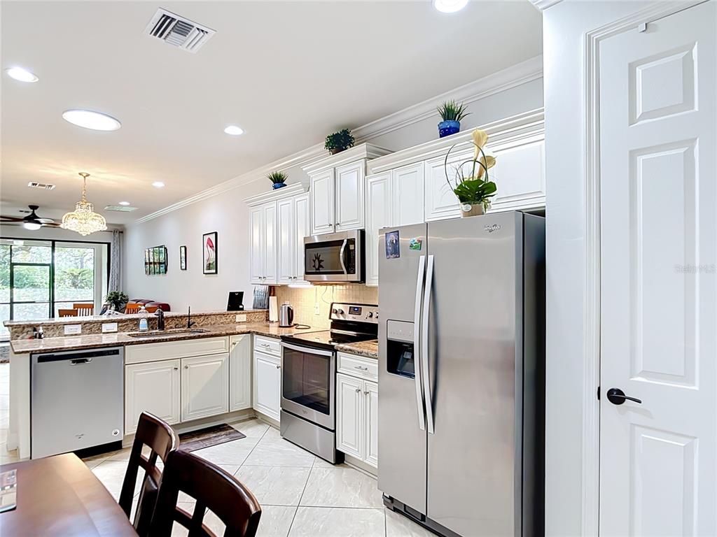 A kitchen features white cabinetry, stainless steel appliances, and granite countertops with tile flooring — 2590 OSWEGO DRIVE, NORTH PORT, FL