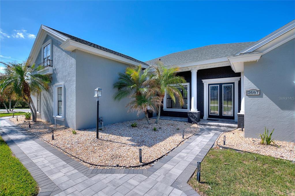 A gray house exterior features a stone walkway, palm trees, and a dark entryway — 2687 BROOKSIDE BLUFF LOOP, LAKELAND, FL
