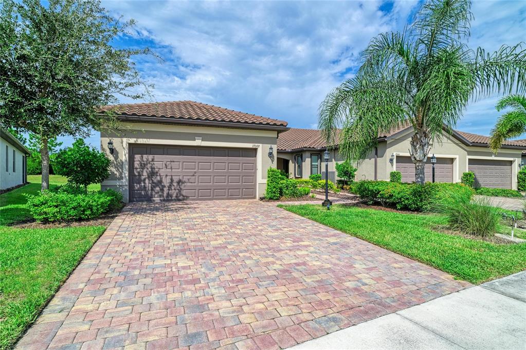 A single-story house with a paved driveway, a three-car garage, and a palm tree — 17648 NORTHWOOD PLACE, LAKEWOOD RANCH, FL