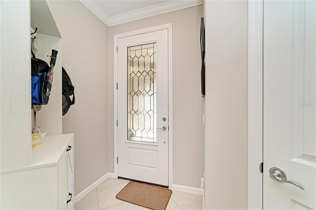 An entryway features a white door with a decorative glass insert, tile flooring, and built-in storage — 17648 NORTHWOOD PLACE, LAKEWOOD RANCH, FL