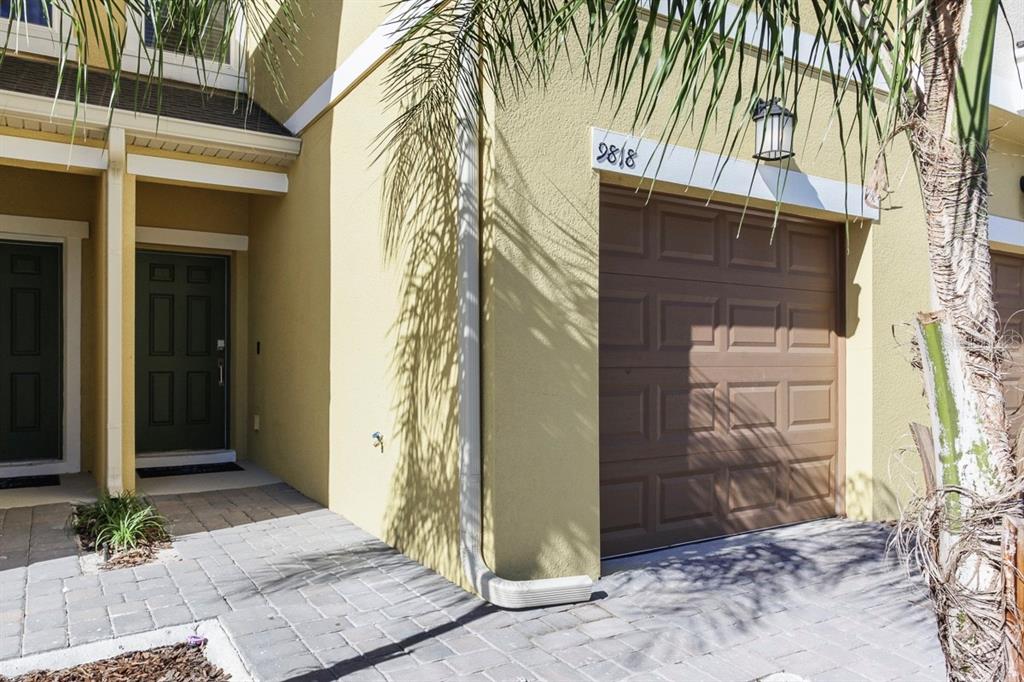 A yellow townhouse exterior features a brown garage door, a dark front door, and pavers — 9818 RED EAGLE DRIVE, ORLANDO, FL