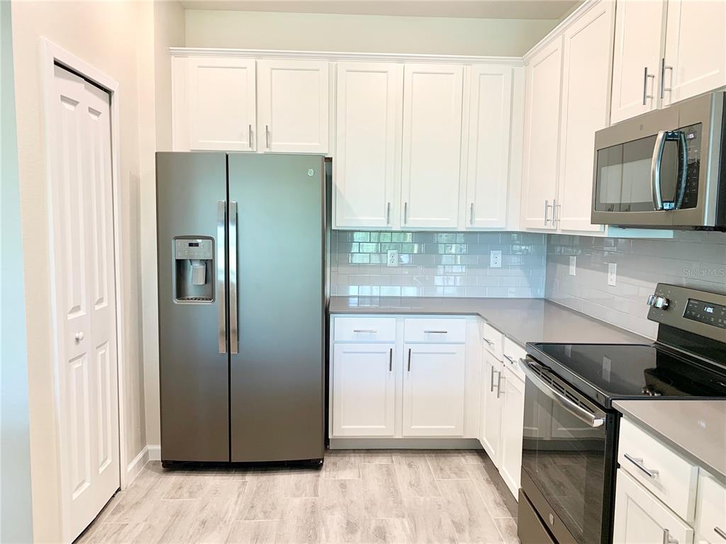 A kitchen features white cabinetry, stainless steel appliances, gray countertops, and a gray subway tile backsplash — 9818 RED EAGLE DRIVE, ORLANDO, FL