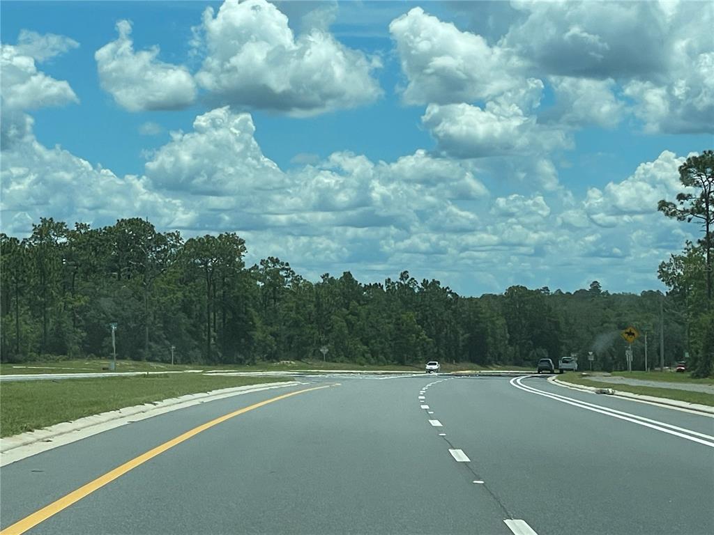 A paved road leads toward a treeline under a bright blue sky with large clouds — 00 SR 20, INTERLACHEN, FL