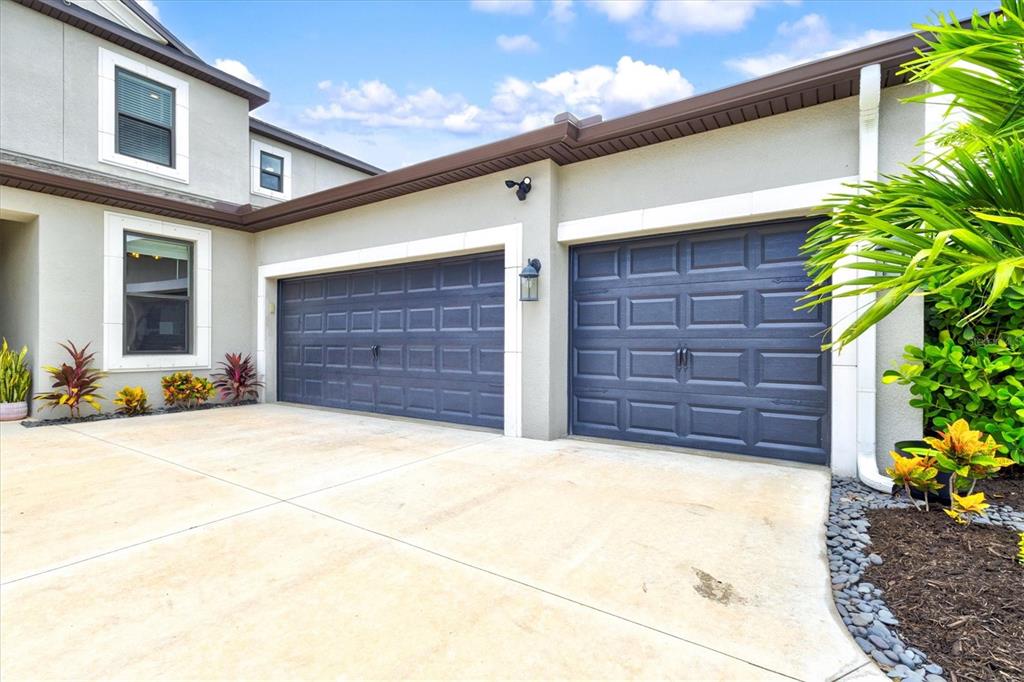 A beige house exterior features a covered entryway, a dark garage door, and landscaping — 9297 TEQUILA SUNRISE DRIVE, SARASOTA, FL