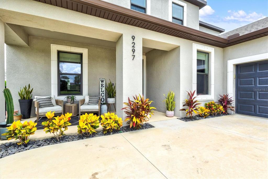 A covered front porch features a dark door, two chairs, a rug, and a potted plant — 9297 TEQUILA SUNRISE DRIVE, SARASOTA, FL