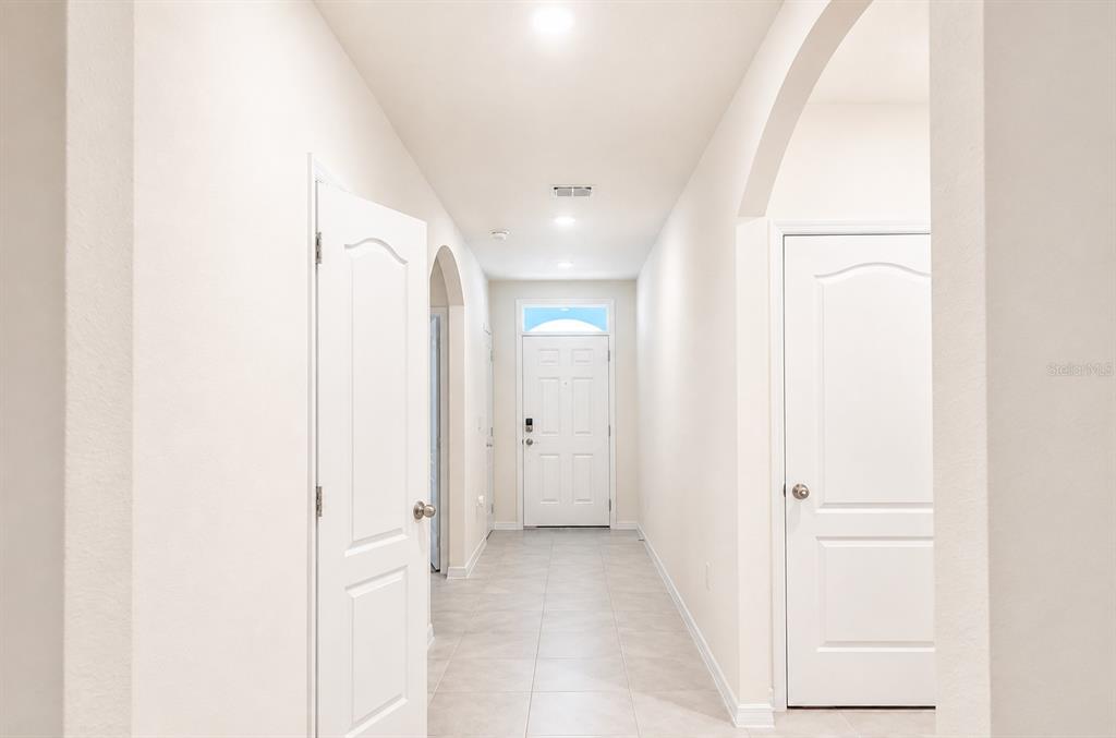 A bright hallway with white walls, tile flooring, and two closed interior doors — 2132 SILVER BROOK WAY, DAVENPORT, FL