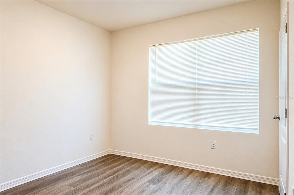 An empty bedroom features light-colored walls, a window with white blinds, and wood-look flooring — 2132 SILVER BROOK WAY, DAVENPORT, FL