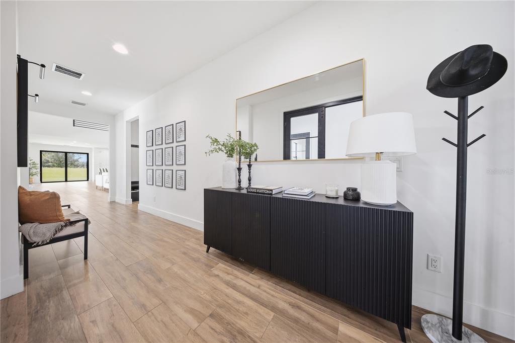 A modern hallway features wood-look flooring, a black console table, a mirror, and a coat rack — 16930 WINTER ROAD, MONTVERDE, FL