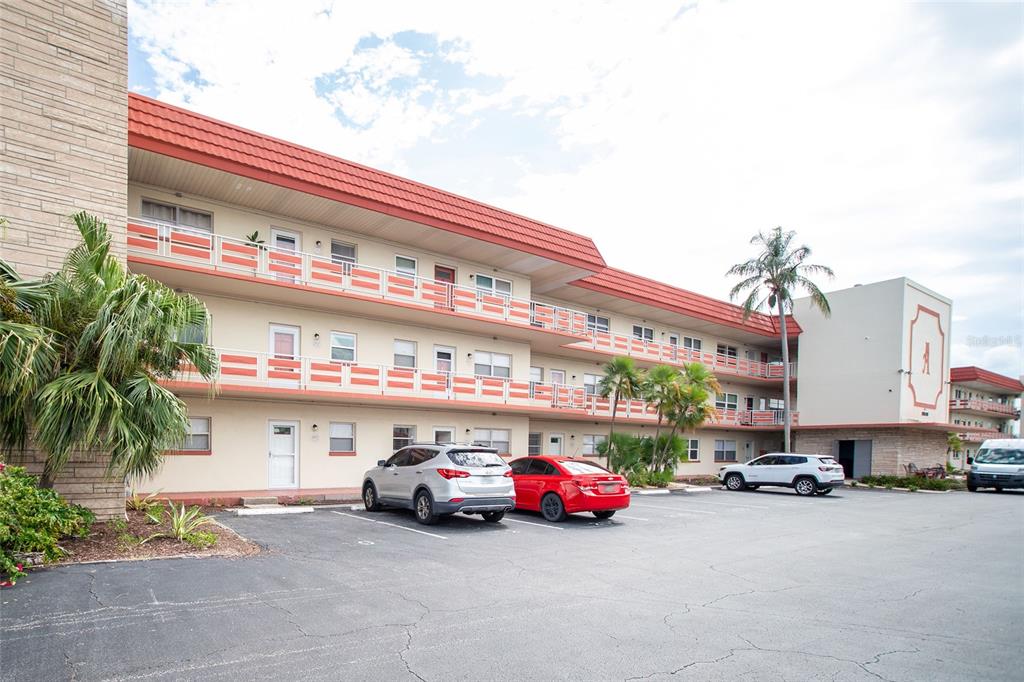 A three-story apartment building with a red roof and exterior walkways sits above a parking lot — 5840 30TH AVENUE S UNIT 202, GULFPORT, FL