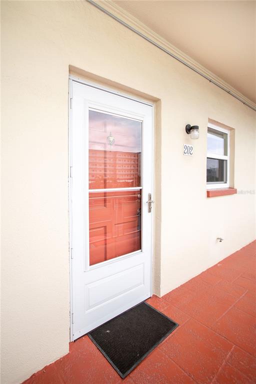 A white exterior door with a glass storm door sits on a red tiled walkway — 5840 30TH AVENUE S UNIT 202, GULFPORT, FL