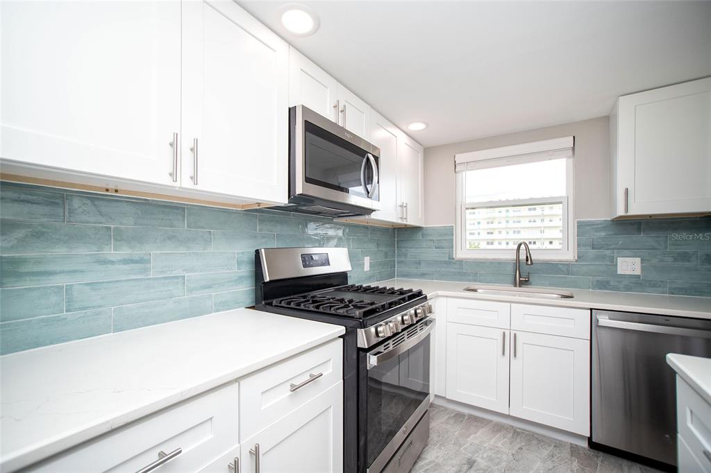 A kitchen with white cabinets, stainless steel appliances, and a blue subway tile backsplash — 5840 30TH AVENUE S UNIT 202, GULFPORT, FL