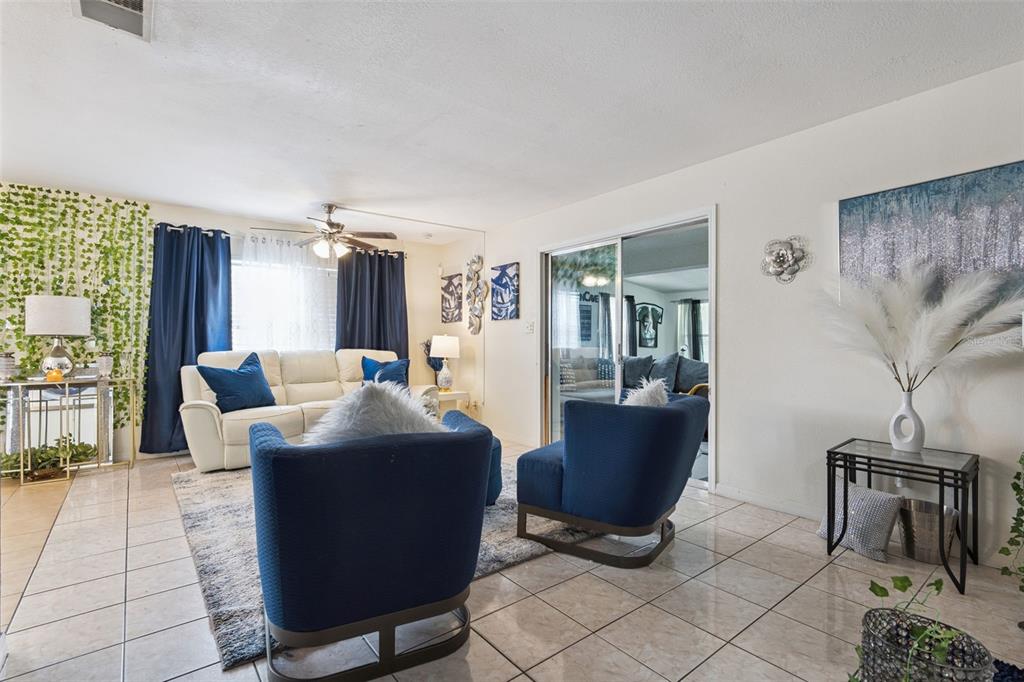 A living room features a white sofa, two blue armchairs, tile flooring, and sliding doors — 1912 SAXON BOULEVARD, DELTONA, FL