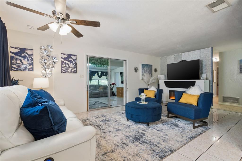 A living room features a white sofa, blue armchairs, a round ottoman, and a fireplace — 1912 SAXON BOULEVARD, DELTONA, FL