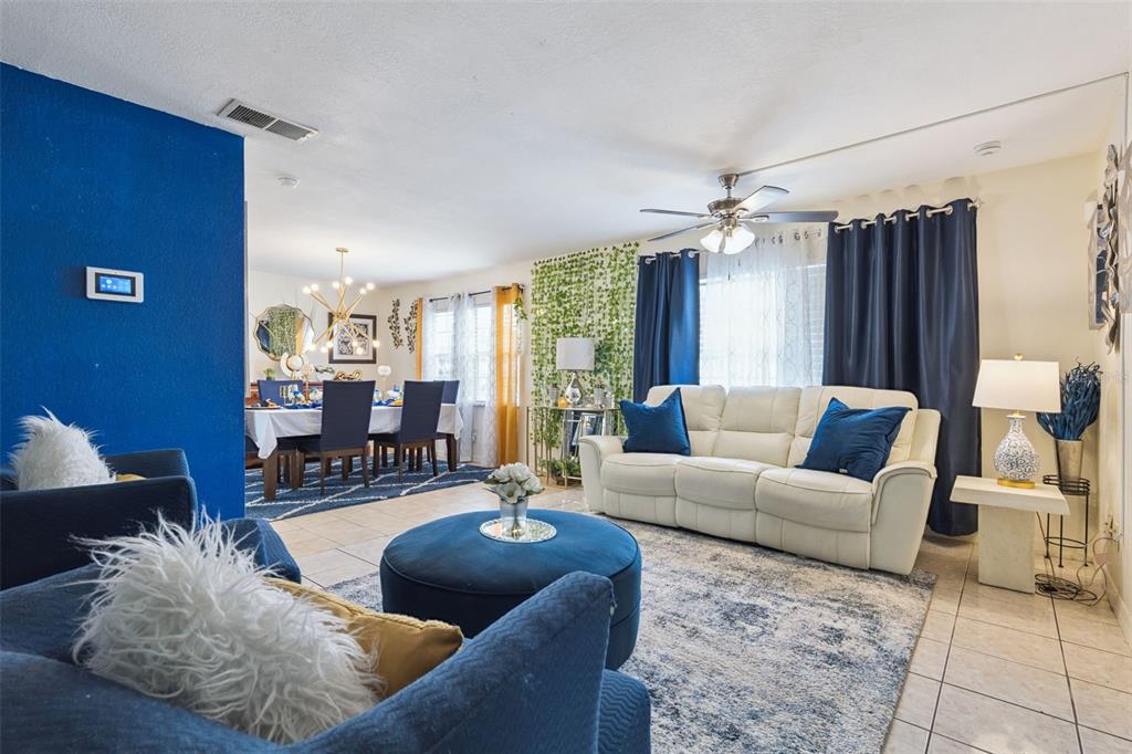 A living room with a white sofa, blue ottoman, and an adjacent dining area — 1912 SAXON BOULEVARD, DELTONA, FL