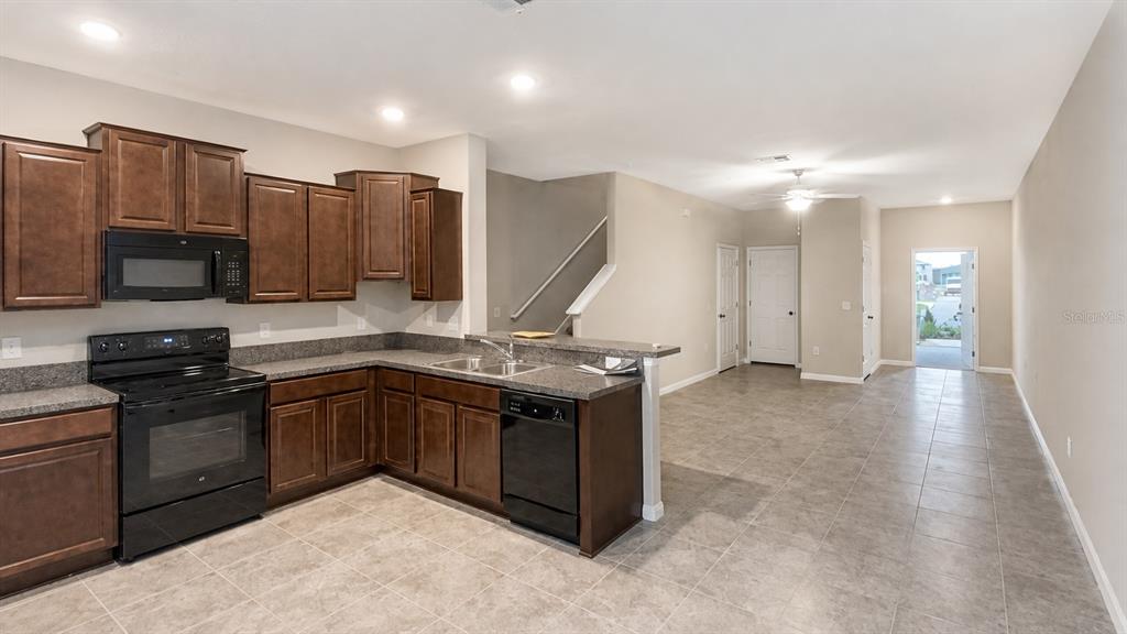 A kitchen with dark wood cabinets, black appliances, and tile flooring opens to a hallway — 3836 CAT MINT STREET, TAMPA, FL