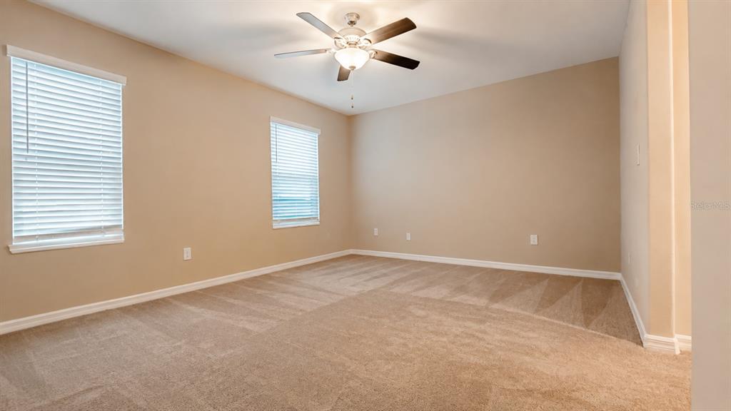 An empty bedroom features beige walls, tan carpeting, two windows with blinds, and a ceiling fan — 3836 CAT MINT STREET, TAMPA, FL