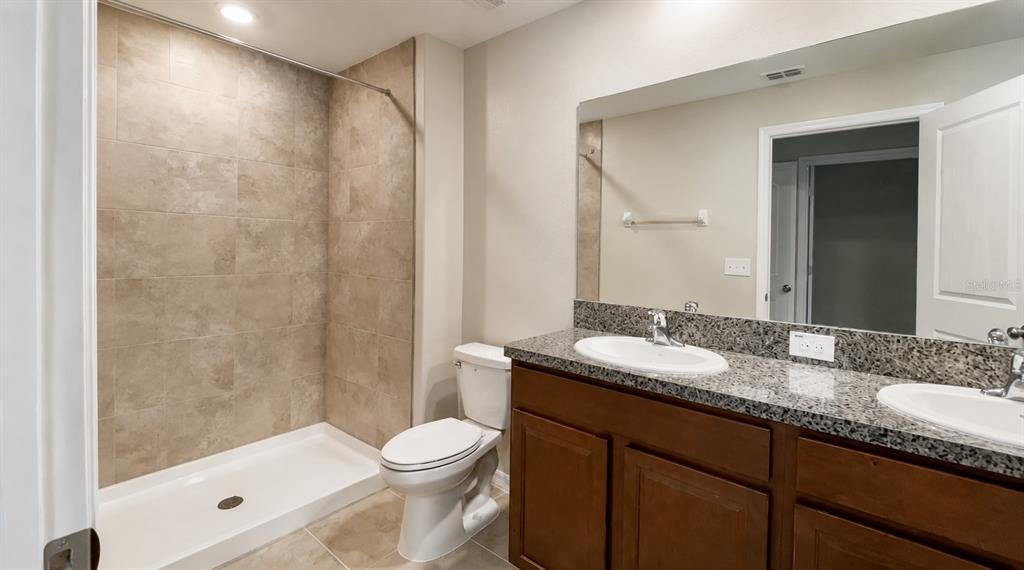 A bathroom with a tiled walk-in shower, a toilet, and a double-sink granite vanity — 3836 CAT MINT STREET, TAMPA, FL