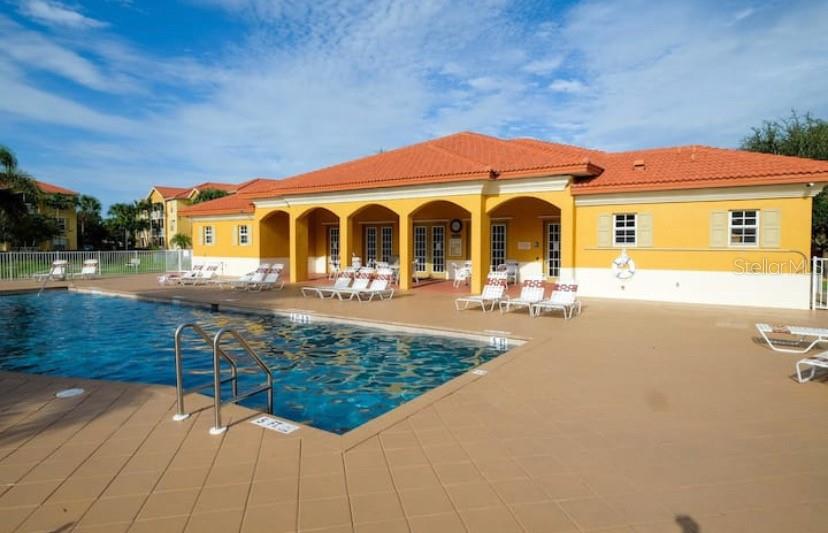A swimming pool sits in front of a yellow clubhouse with a tiled roof — 4149 RESIDENCE DRIVE UNIT 801, FORT MYERS, FL