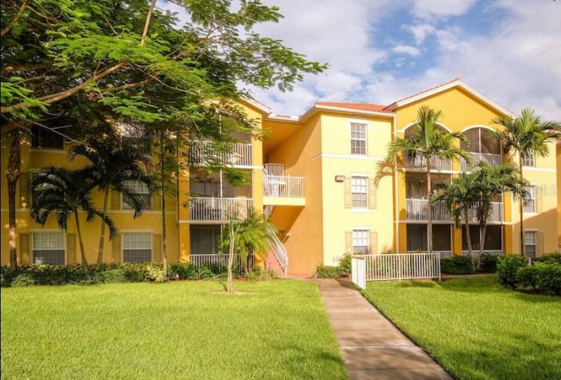 A three-story yellow apartment building with screened balconies and palm trees on a grassy lawn — 4149 RESIDENCE DRIVE UNIT 801, FORT MYERS, FL