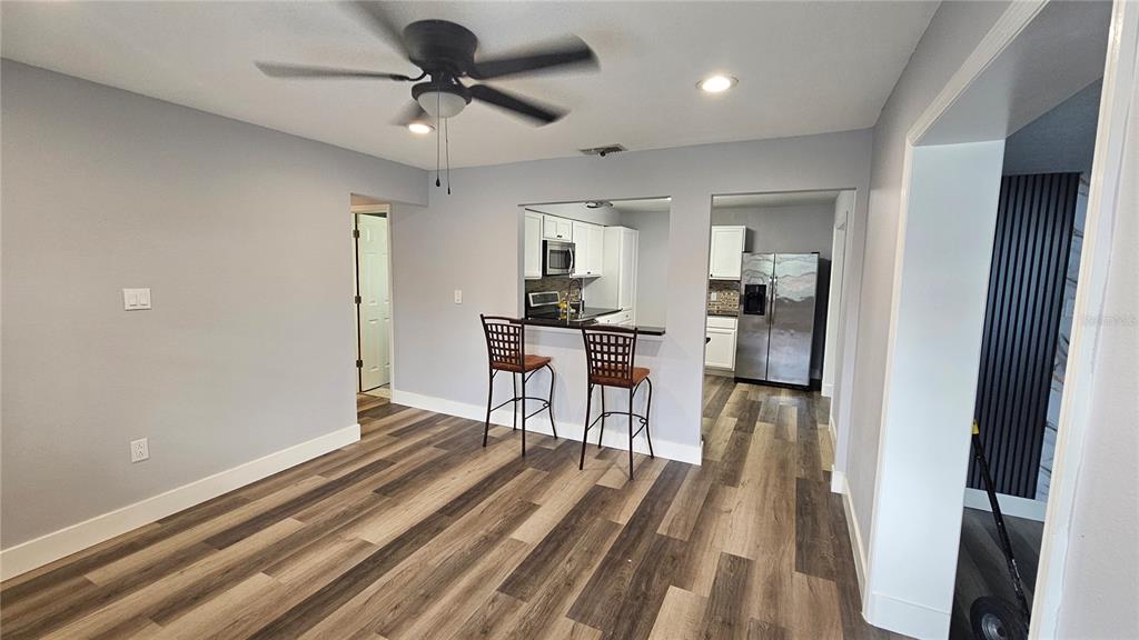 A dining area with wood-look flooring features a breakfast bar opening into a kitchen — 3502 LIBBY LOOP, TAMPA, FL