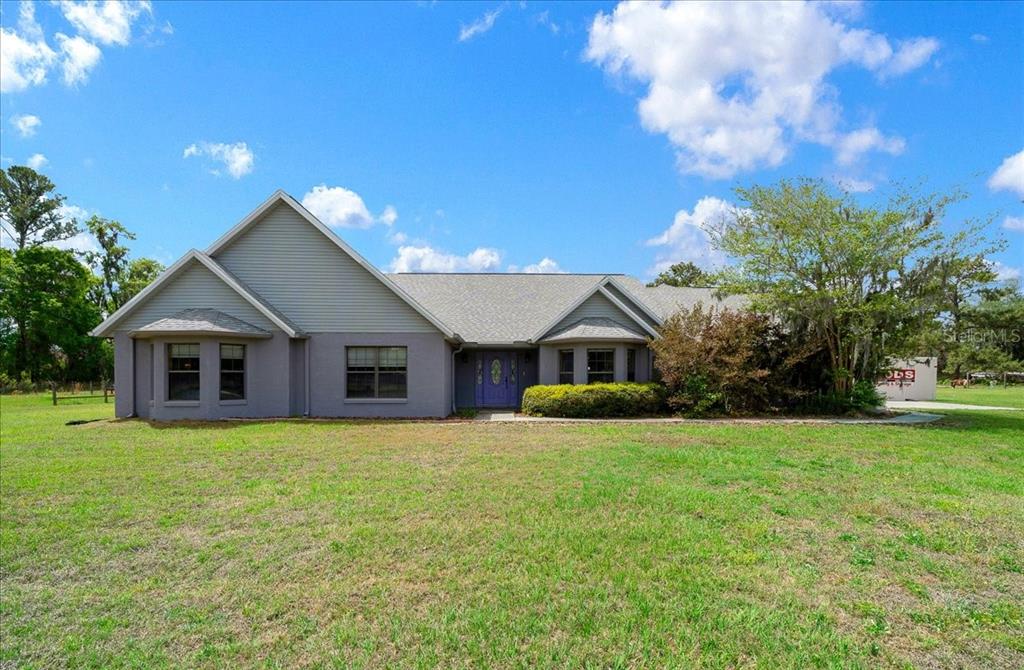 A single-story house with gray siding and a purple front door sits on a lawn — 13456 W HIGHWAY 318, WILLISTON, FL