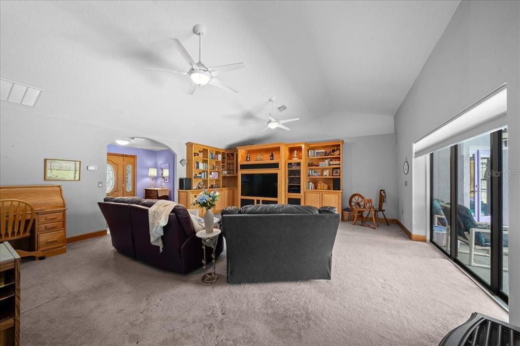 A living room features vaulted ceilings, two ceiling fans, built-in wooden cabinetry, and carpeted floors — 13456 W HIGHWAY 318, WILLISTON, FL