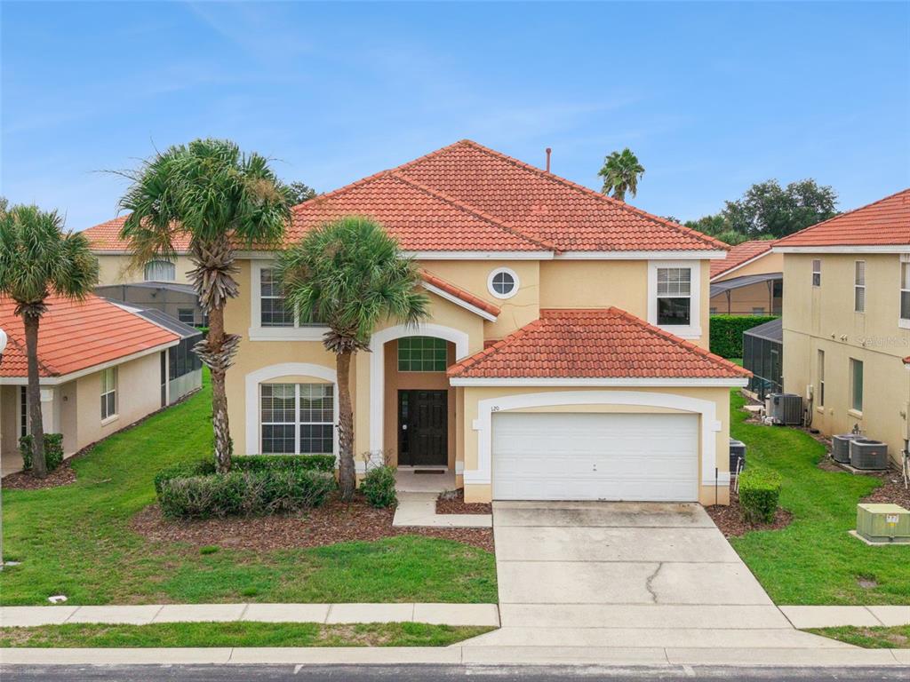 A two-story suburban house with a red tile roof, tan stucco siding, and a garage — 120 SARAGOSSA AVENUE, DAVENPORT, FL