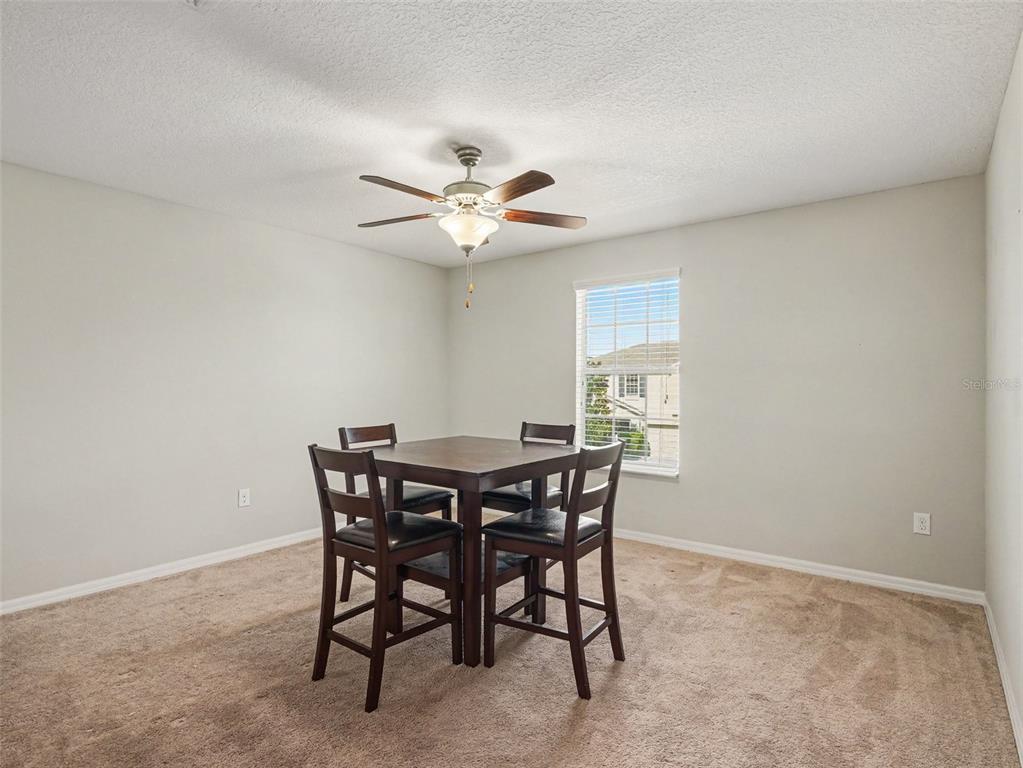 The rear exterior of a two-story beige house with a small patio and lawn — 2210 PURPLE ORCHID PLACE, RUSKIN, FL