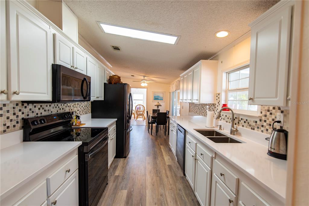 A galley kitchen features white cabinets, black appliances, quartz countertops, and a mosaic tile backsplash — 15 ROTTERDAM DRIVE, PUNTA GORDA, FL