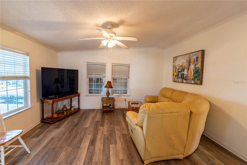 A living room features wood-look flooring, a large television, a yellow sofa, and a ceiling fan — 15 ROTTERDAM DRIVE, PUNTA GORDA, FL