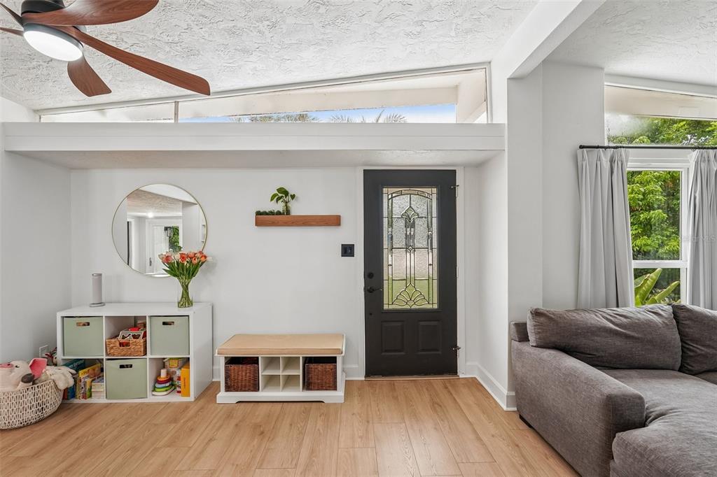An entryway features a dark front door, white storage units, a round mirror, and wood flooring — 2406 FLORIDA BOULEVARD, BRADENTON, FL