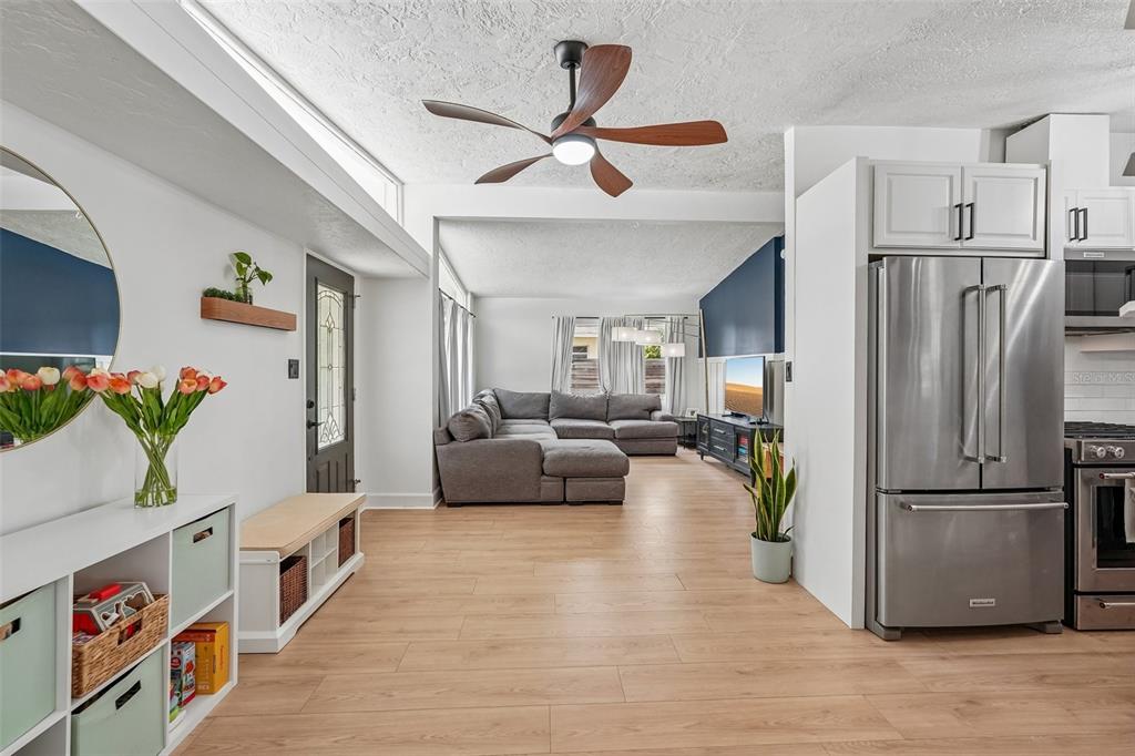 An open-concept living area features light wood flooring, a gray sectional sofa, and a kitchen — 2406 FLORIDA BOULEVARD, BRADENTON, FL