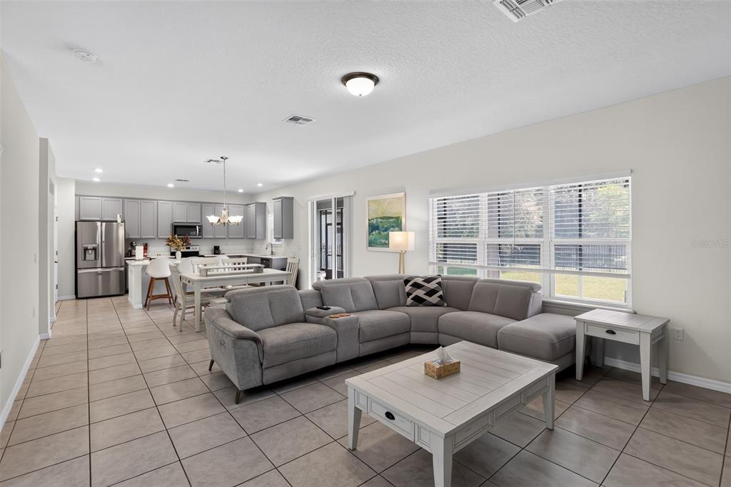 An open-concept living room and kitchen featuring gray cabinetry, tile flooring, and a sectional sofa — 3145 JADE TREE POINT, OVIEDO, FL