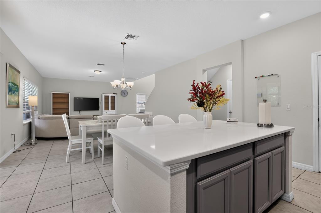 A kitchen island with a white countertop overlooks an open-concept dining and living area — 3145 JADE TREE POINT, OVIEDO, FL