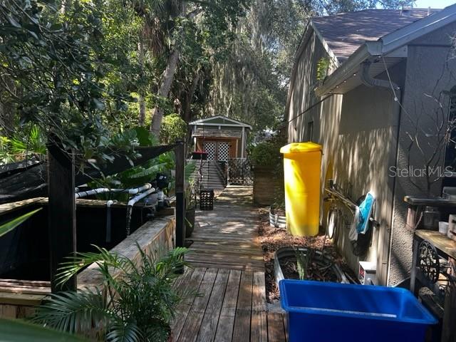A wooden walkway leads past a large fish tank and a yellow bin toward a shed — 5781 AUTUMN CHASE CIRCLE, SANFORD, FL