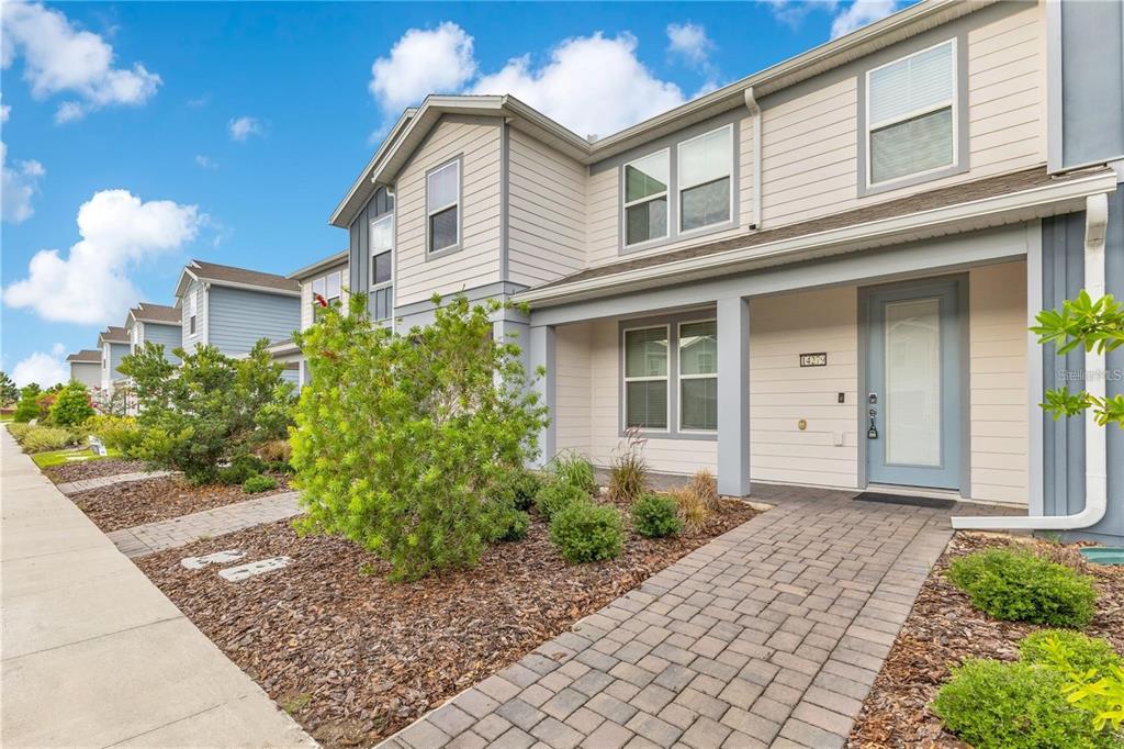 A two-story townhouse exterior with light siding, a paved walkway, and a small front garden — 14279 SAPELO BEACH DRIVE, ORLANDO, FL