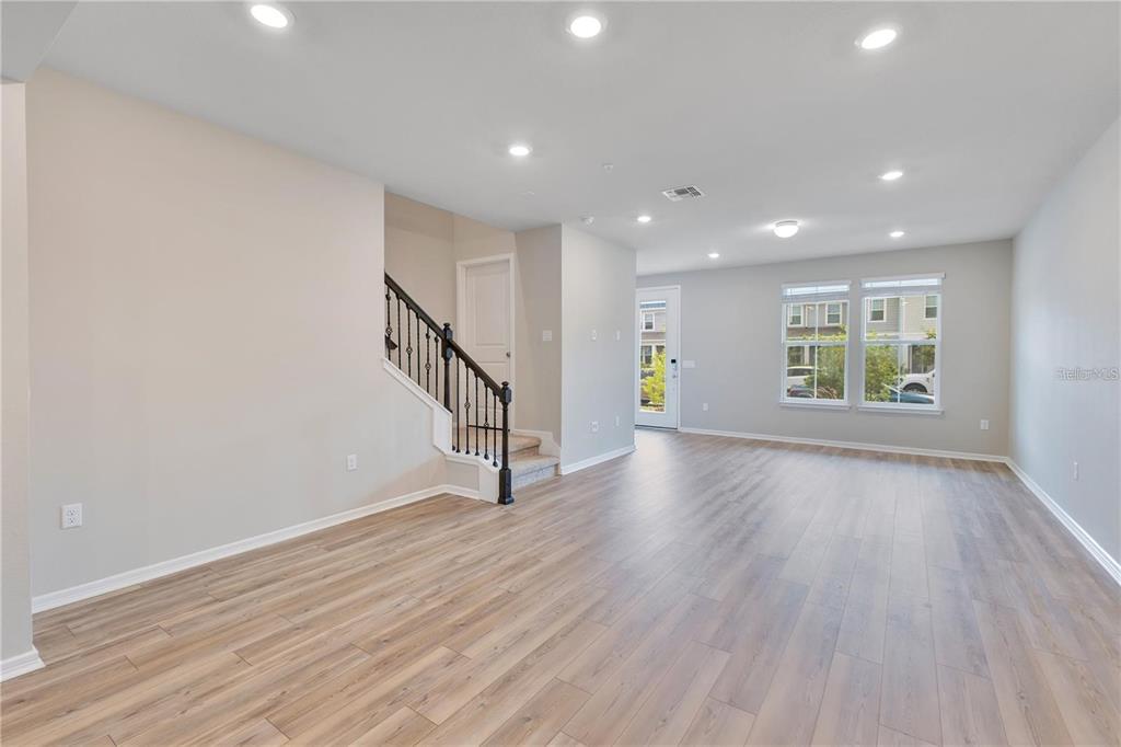 An open living area features light wood-look flooring, recessed lighting, and a staircase with black railings — 14279 SAPELO BEACH DRIVE, ORLANDO, FL