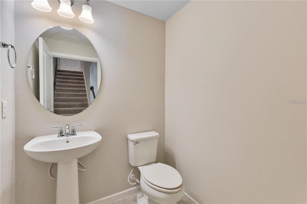 A half bathroom features a pedestal sink, a round mirror, and a white toilet — 14279 SAPELO BEACH DRIVE, ORLANDO, FL