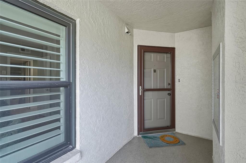 A covered entryway features a window with blinds, a storm door, and a welcome mat — 1328 PASADENA AVENUE S UNIT 308, SOUTH PASADENA, FL